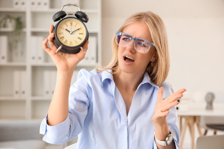 Stressed young businesswoman with alarm clock working under deadline in office, closeupの写真素材