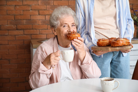 Young woman with her grandmother eating buns in kitchenの写真素材