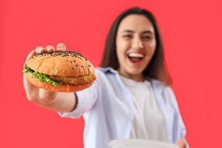 Young woman with tasty burger on red background, closeupの写真素材