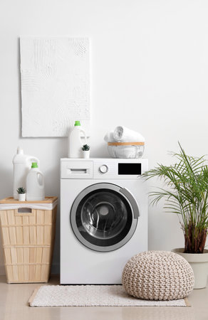 Washing machine with bottles of detergent, laundry basket and pouf near white wallの写真素材