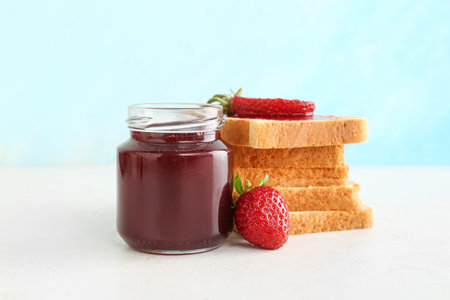 Jar of sweet strawberry jam and tasty toasts on table