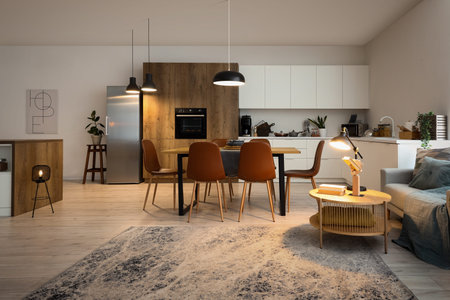 Interior of modern open plan kitchen with dining table and glowing lampsの写真素材