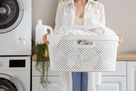 Woman with basket of dirty clothes in laundry room with washing machinesの写真素材