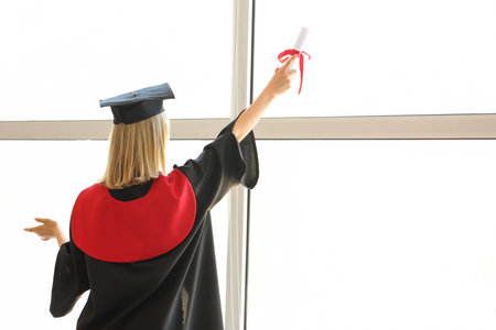 Female graduate student with diploma near window in room, back viewの写真素材