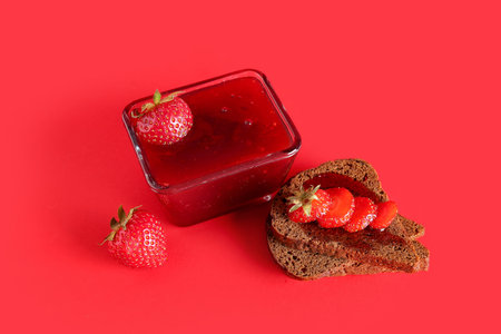 Bowl with sweet strawberry jam and bread on red background