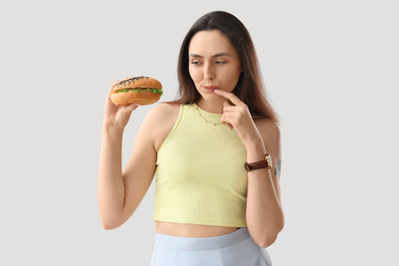 Thoughtful young woman with tasty burger on light backgroundの写真素材
