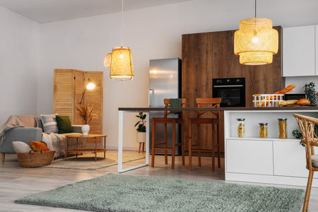 Interior of modern open space kitchen with gray sofa, island and glowing lamps