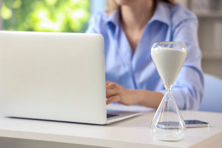 Hourglass on table of businesswoman working in office, closeupの写真素材