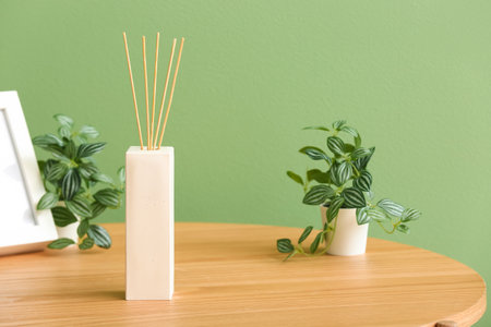 Bottle of reed diffuser and houseplants on table near color wall in roomの写真素材