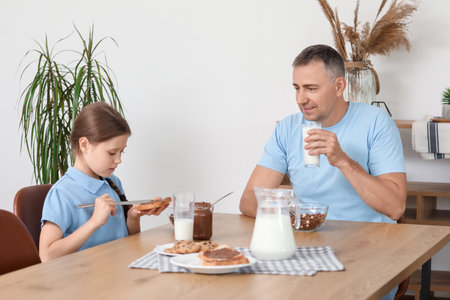 Little girl and her father having breakfast with fresh milk in living roomの写真素材