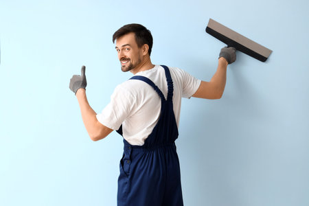Male decorator with putty knife on blue background