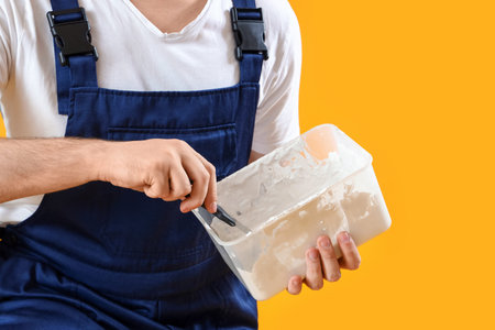 Male decorator with putty knife and plaster on yellow background, closeup