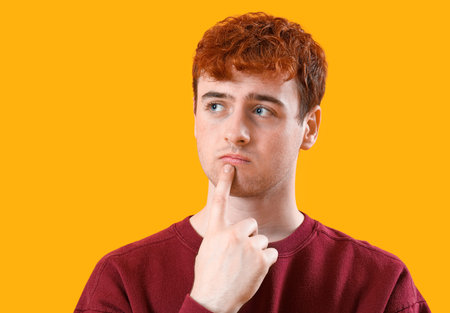 Thoughtful young redhead man on yellow background, closeup
