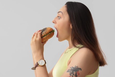 Young woman eating tasty burger on light background, closeupの写真素材