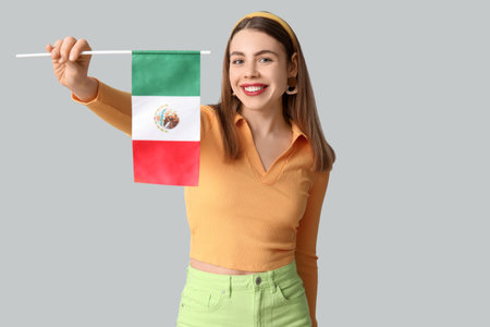 Happy young woman with Mexican flag on gray backgroundの写真素材