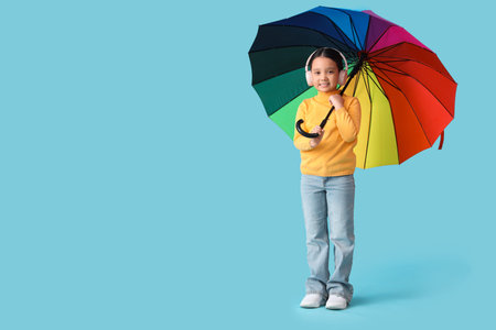 Portrait of fashionable little girl with headphones and umbrella on blue backgroundの写真素材