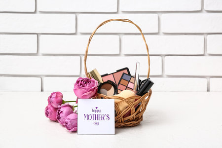 Gift basket with decorative cosmetics, rose flowers and card for Mother's Day celebration on table near light brick wallの写真素材