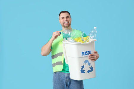 Male volunteer in reflective vest holding recycle bin with plastic on blue background