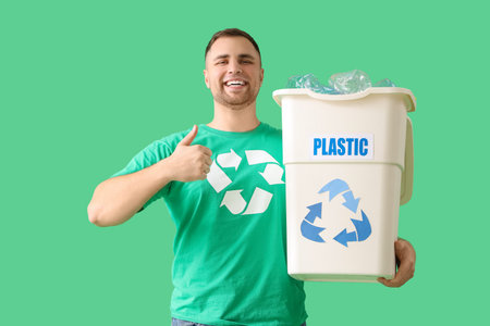Male volunteer with recycle bin for plastic showing thumb-up on green background