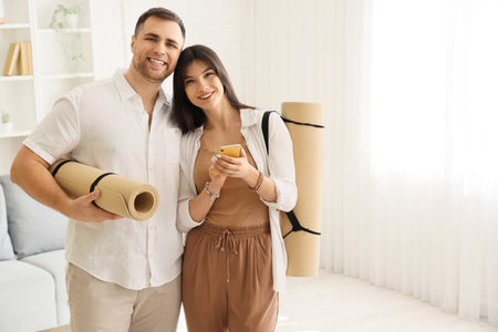 Sporty young couple with yoga mats and mobile phone in light living room