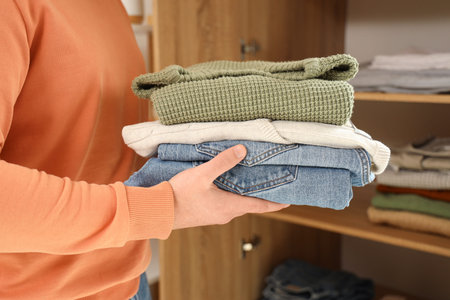 Young man putting stack of clothes into closet at home, closeup