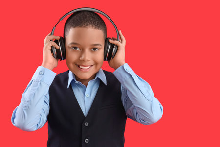 Happy little African-American schoolboy in headphones on red backgroundの写真素材
