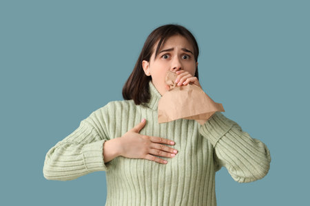 Beautiful young stressed woman with paper bag having panic attack on blue background. Stress Awareness Monthの写真素材
