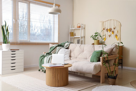 Comfortable sofa with plaid, coffee table with laptop and bamboo plant in living roomの写真素材
