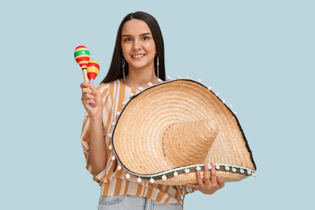 Beautiful young woman with sombrero hat and maracas on blue background