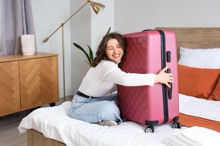 Happy female tourist hugging suitcase on bed in hotel roomの写真素材