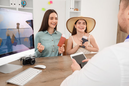 Young lesbian couple with passports sitting at table in travel agencyの写真素材