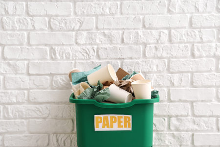 Green recycling bin with paper near white brick wall. Recycle conceptの写真素材