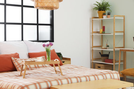Interior of comfortable bedroom with bed, window, shelving unit and tray with tulipsの写真素材