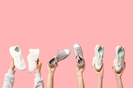 Female hands with different stylish sneakers on pink backgroundの写真素材
