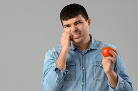 Young man with tomato suffering from toothache on light background, closeupの写真素材