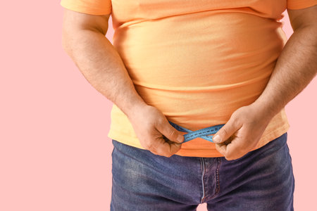 Overweight mature man with measuring tape on pink background, closeup. Weight loss conceptの写真素材