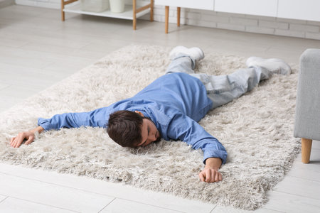 Tired young man lying on carpet at homeの写真素材