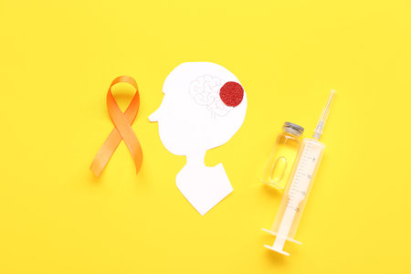 Paper human head with syringe and orange ribbon on yellow background. Multiple Sclerosis Awareness Monthの写真素材