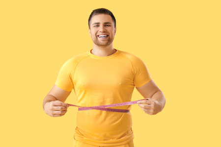 Young man measuring his waist on yellow background. Weight loss conceptの写真素材