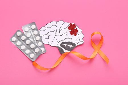 Paper brain with puzzle piece, pills and orange ribbon on pink background. Multiple Sclerosis Awareness Monthの写真素材