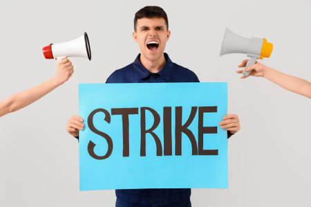 Protesting mechanic holding placard with word STRIKE and megaphones on light backgroundの写真素材