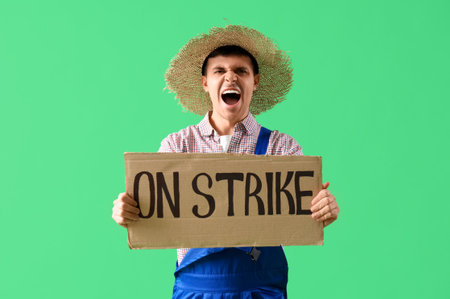 Protesting male farmer holding placard with text ON STRIKE against green backgroundの写真素材