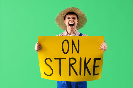 Protesting male farmer holding placard with text ON STRIKE against green backgroundの写真素材