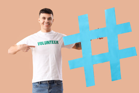 Handsome male volunteer pointing at hashtag sign on color backgroundの写真素材