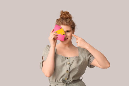 Beautiful young woman pointing at credit cards on gray backgroundの写真素材