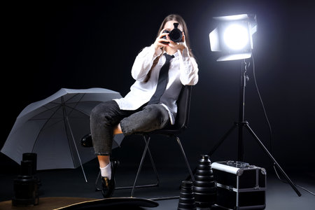 Female photographer with modern camera and lighting equipment taking picture of viewer on black backgroundの写真素材