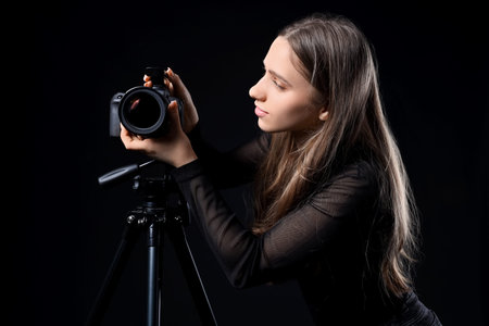 Portrait of female photographer with modern camera on tripod against black background