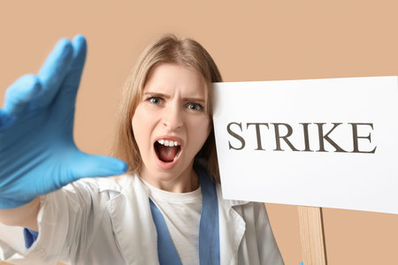 Protesting female doctor holding placard with text STRIKE on beige background, closeup