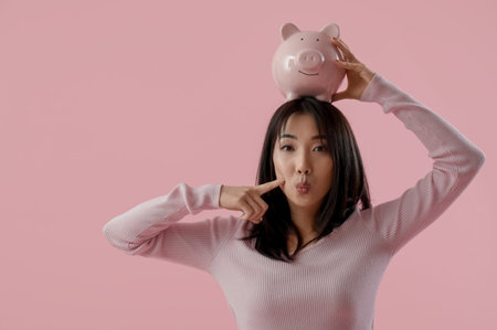 Asian young woman with piggy bank on pink backgroundの写真素材