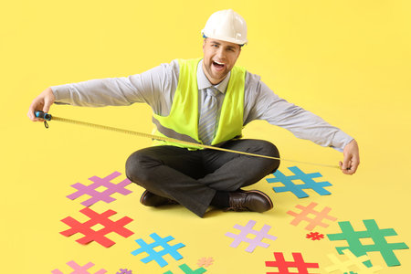 Male architect with tape measure and hashtags sitting on yellow backgroundの写真素材